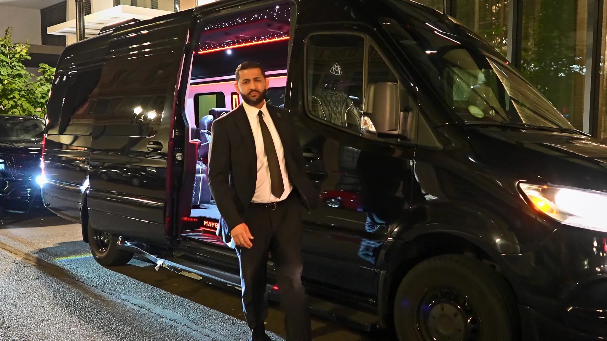 Chauffeur at the open door of the Sprinter Jet Limousine on a downtown street at night