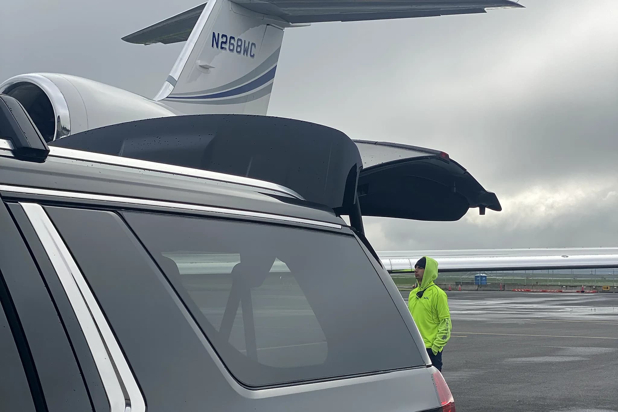 Cadillac Escalade with liftgate open beside a private jet tail — luggage handoff on the FBO ramp