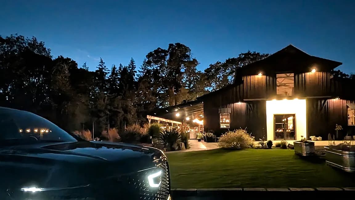 Cadillac Escalade with headlights on at dusk outside a lit estate — evening chauffeur pickup