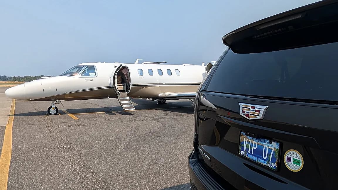 Rear of a Cadillac Escalade beside a private jet in evening light — private aviation chauffeur transfer