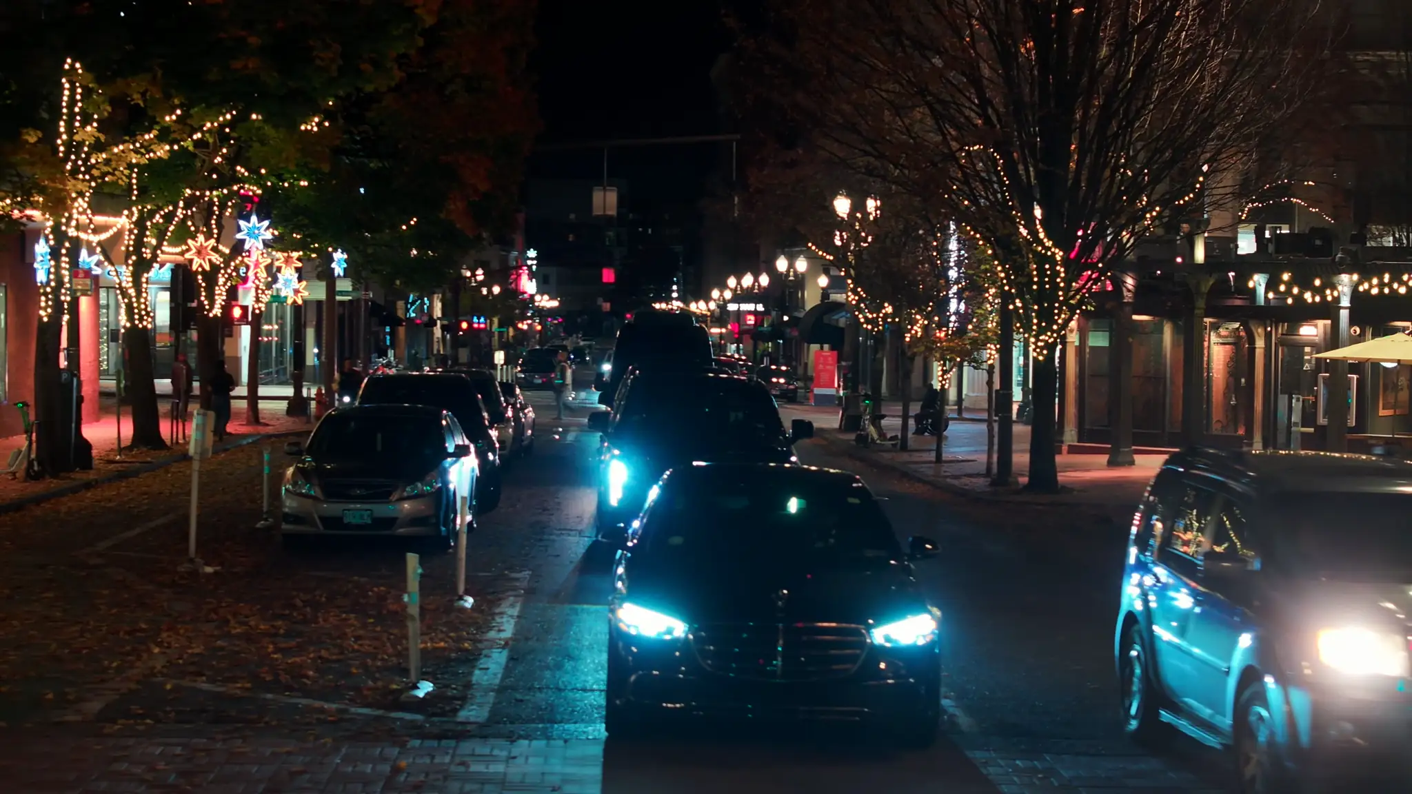 Black chauffeured vehicles with headlights on along a tree-lined downtown Portland street at night