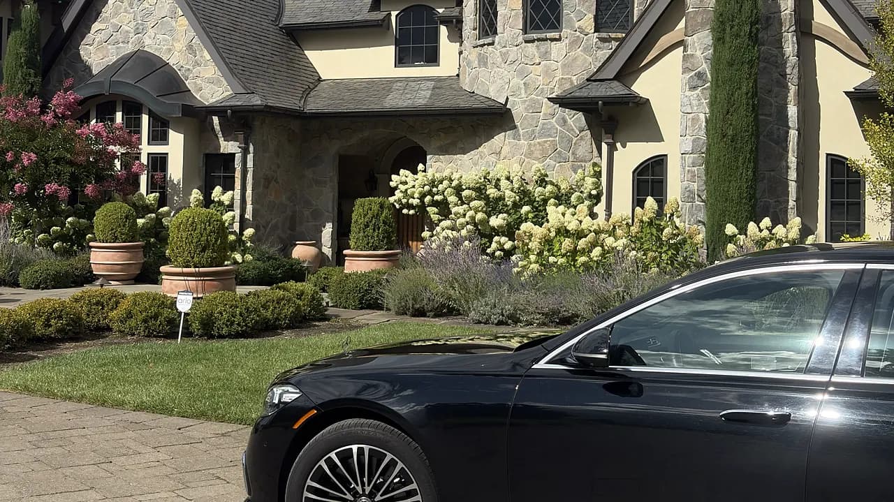 Black chauffeured sedan on the paved driveway of a stone estate with turret and gardens — wedding venue arrival