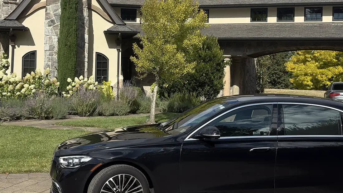 Black chauffeured sedan in front of a stone estate house with gardens — wedding venue arrival