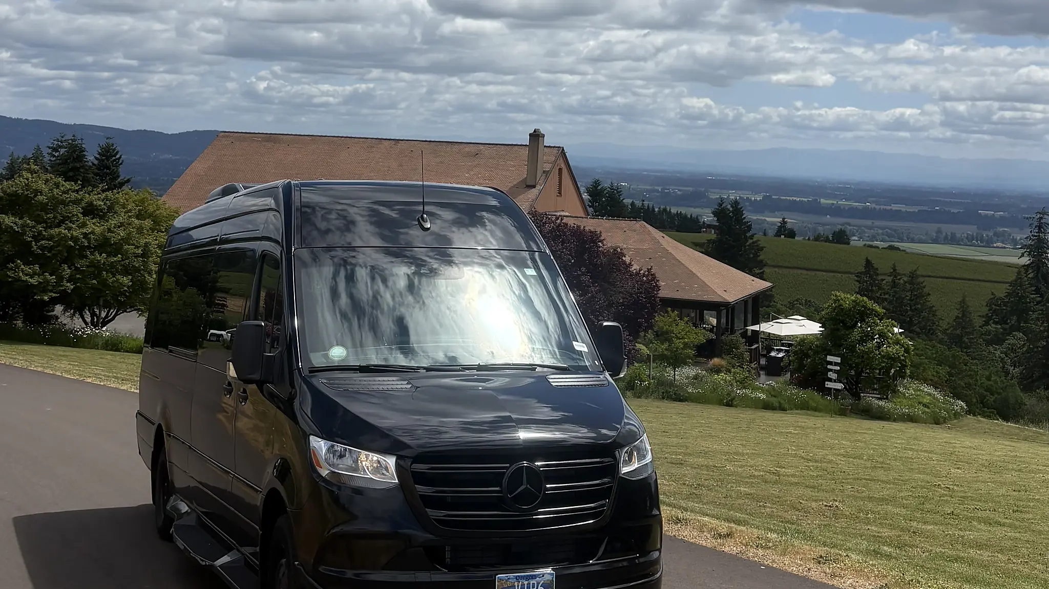 Mercedes-Benz Sprinter on a hillside drive with vineyard and valley view — wine tour chauffeur service