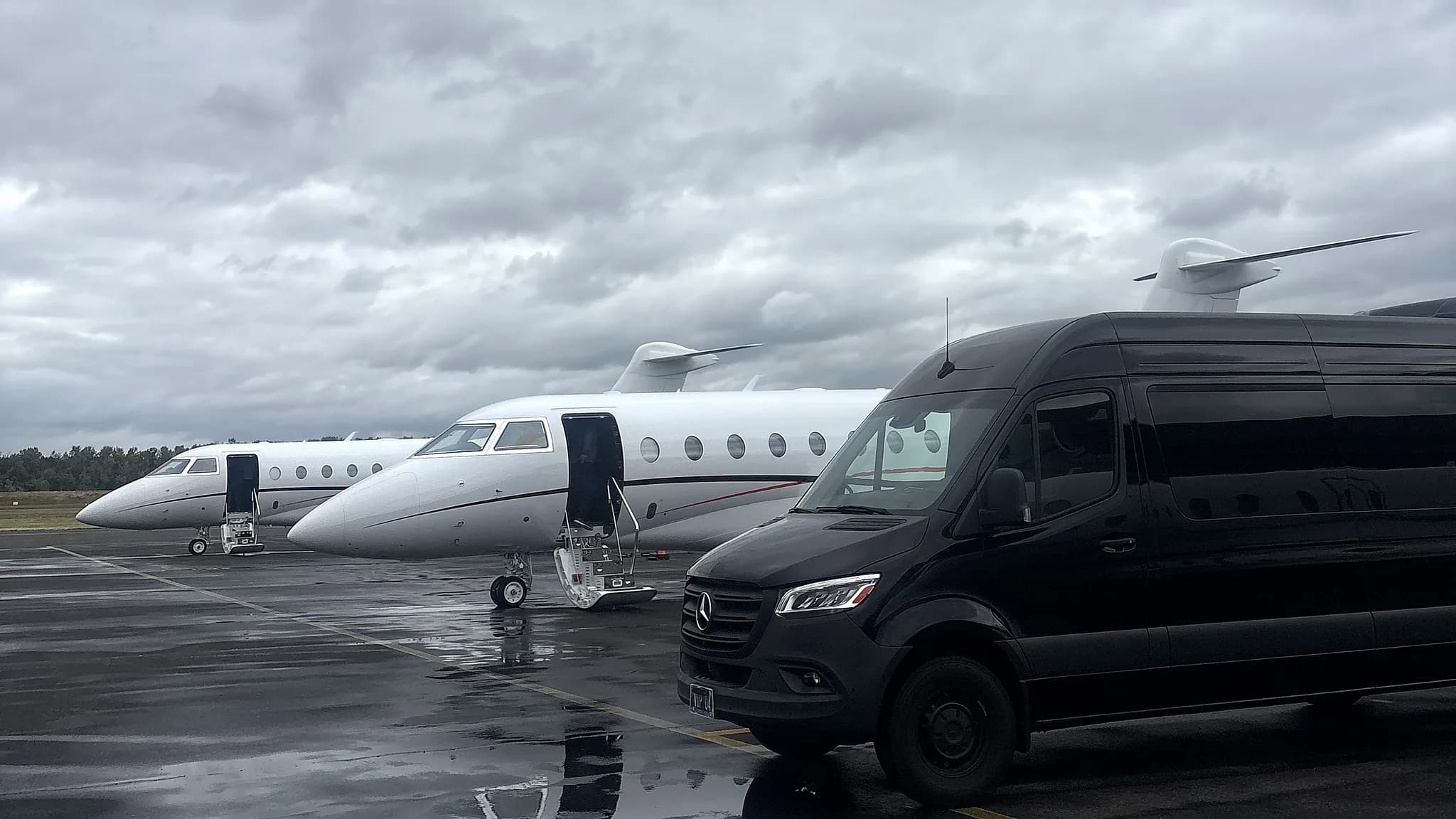 Mercedes-Benz Sprinter beside a private jet on an overcast ramp — group FBO transfer