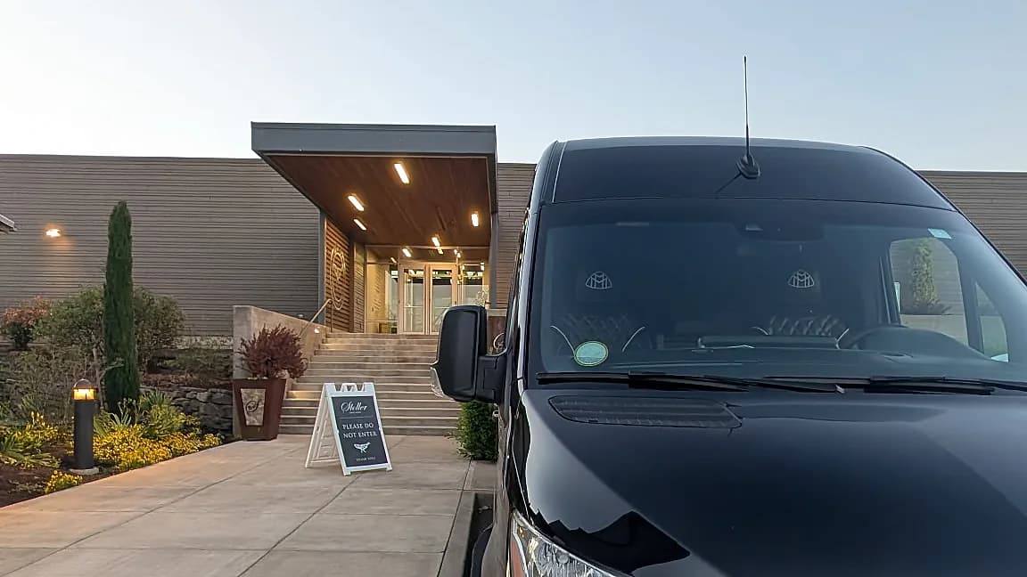 Mercedes-Benz Sprinter parked at a modern venue entrance at dusk — wedding guest shuttle arrival