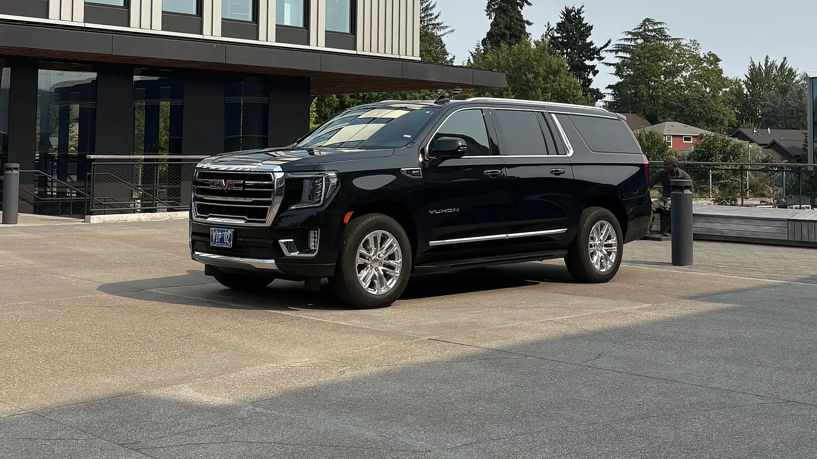 Black chauffeured SUV parked outside a glass office tower — tech-corridor executive transportation