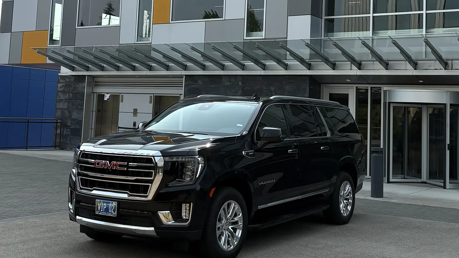 Black chauffeured SUV outside a modern office building entrance — corporate account pickup