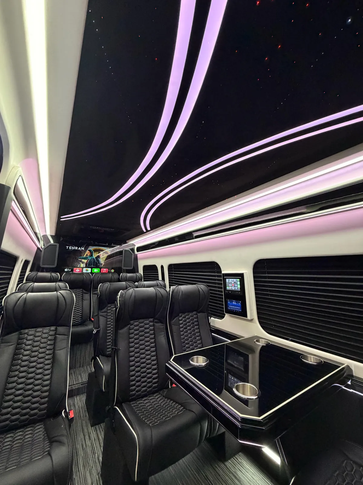 Portland Executive Limo cabin under violet LED accent lighting with the starlight headliner overhead, quilted leather captain chairs, and the bulkhead flat-screen lit