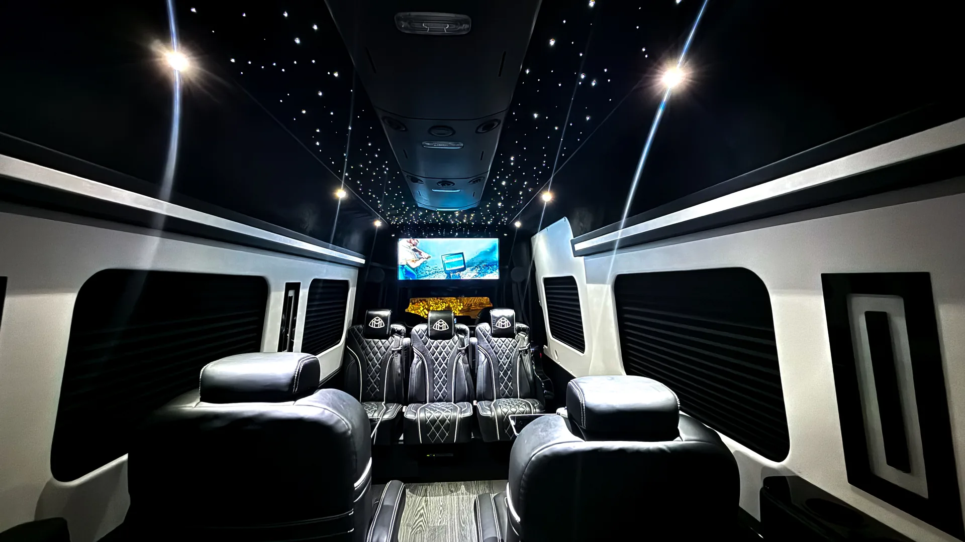 VIP Lounge Sprinter cabin: starlight ceiling, diamond-quilted captain chairs with Maybach headrest emblems facing each other, the rear bench, and the rear screen