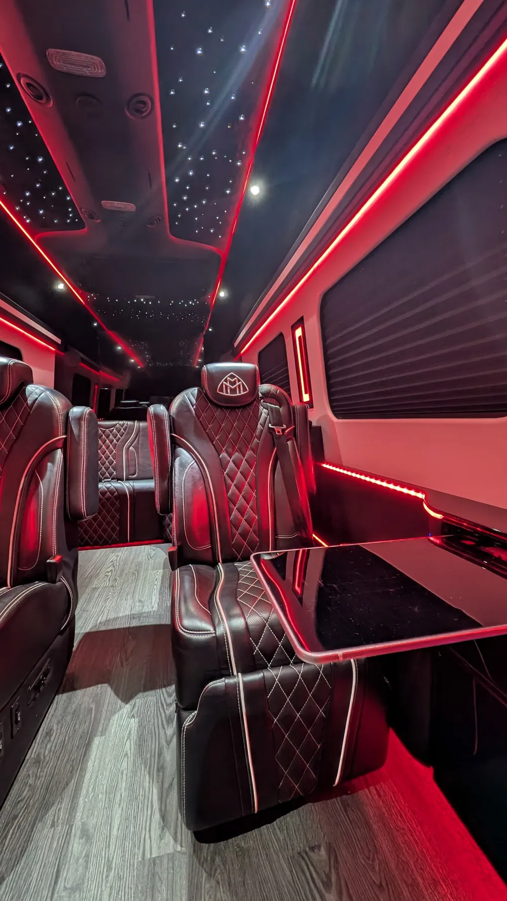 VIP Lounge Sprinter cabin under red LED: the fold-out gloss-black table beside a captain chair, the rear bench, and the starlight ceiling