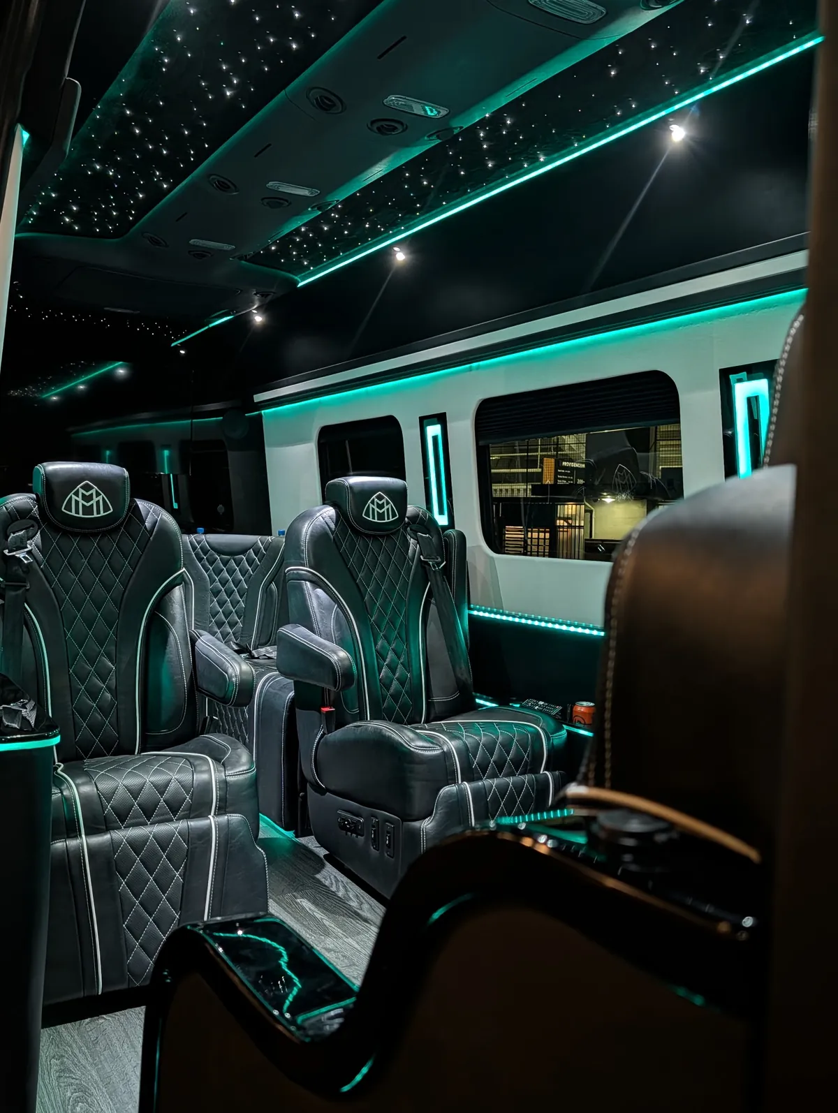 VIP Lounge Sprinter captain chairs in diamond-quilted black leather with white piping and Maybach headrest emblems, lit window accent panels, and the starlight ceiling under teal LED