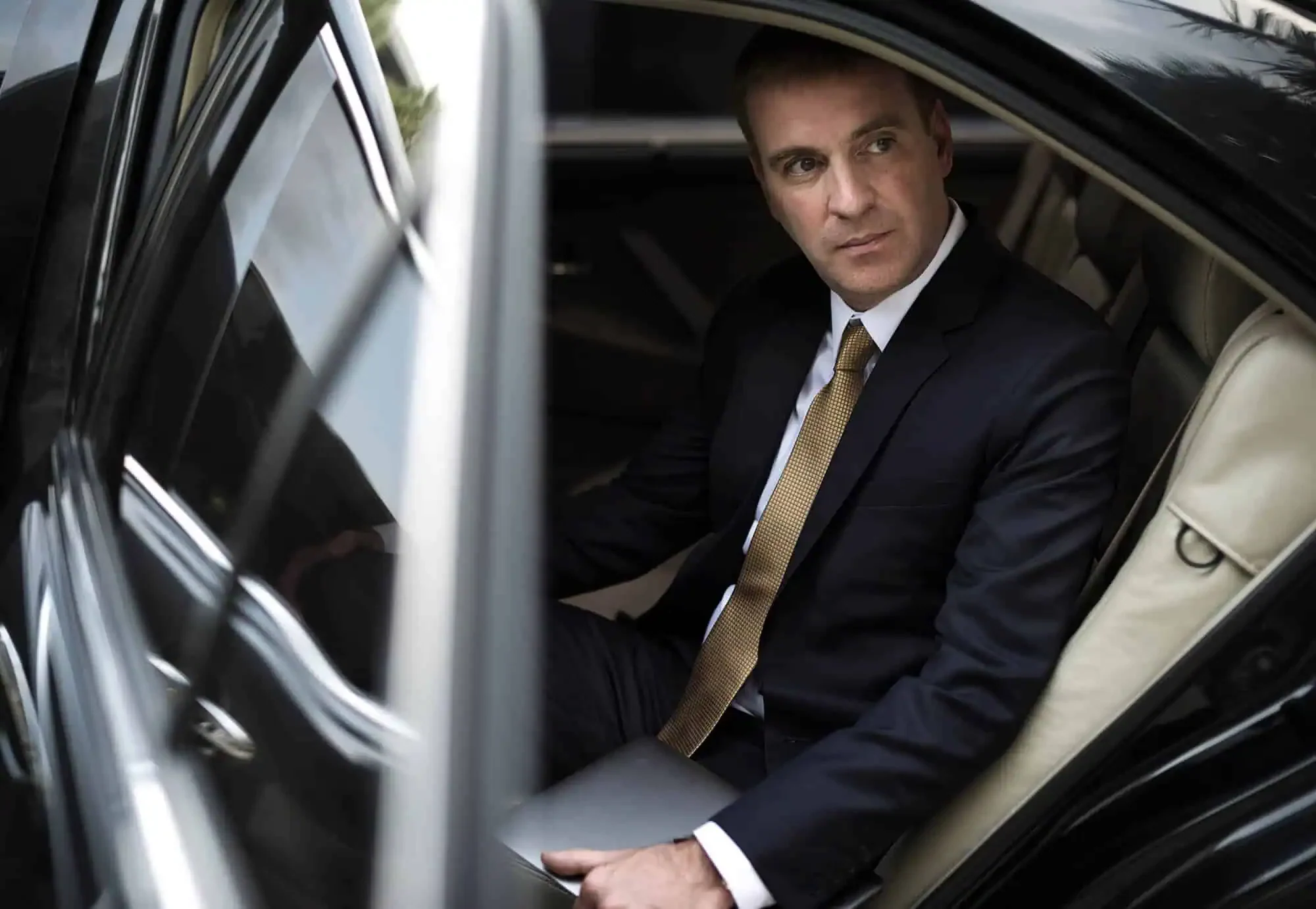 Passenger in a suit seated in the rear of a black sedan with a laptop, working between Portland pickups