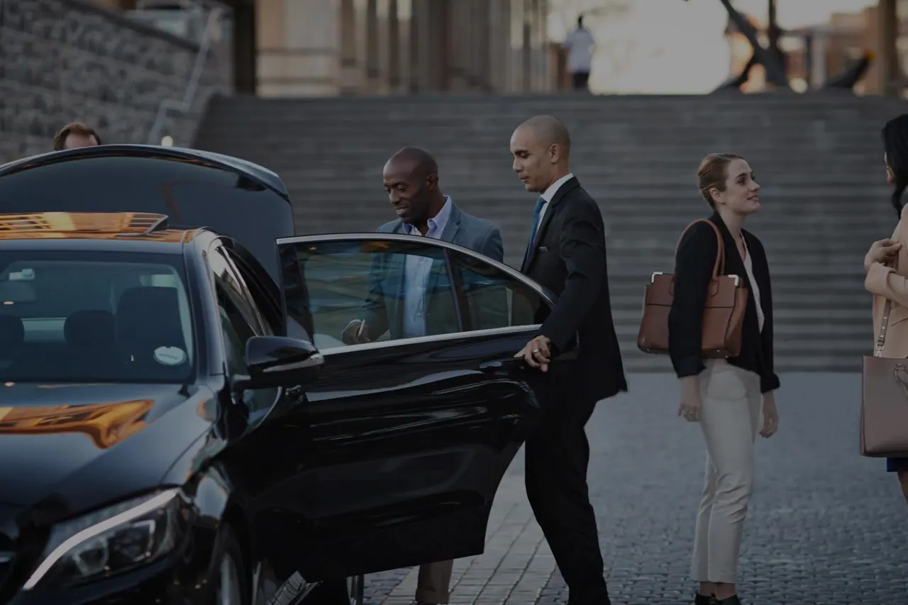 C-Suite Executives & Corporate Teams A chauffeur holding a car door open for a passenger on a city street, illustrating Portland corporate car service
