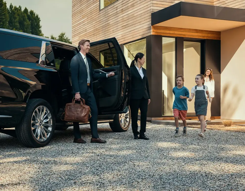 Visiting Professionals & Relocating Families A chauffeur holding an SUV door as a family leaves a house, illustrating Portland service for visiting professionals and relocating families